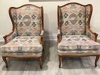 Front view of both wingback chairs side by side on wood floor, showing patterned upholstery and curved wood frames.