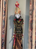 Front view of the vintage Indonesian wooden wayang puppet featuring intricate headgear, detailed painted face, and traditional fabric clothing with beadwork.