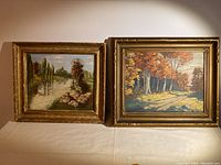 Two framed oil paintings pictured side by side showing autumn forest landscape and river scene