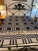 Full view of coverlet spread on a metal bed frame showing the geometric woven pattern and one fringed border.