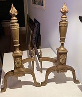 Pair of antique burned bronze and wrought iron andirons displayed on table, showing full front view and curved feet.