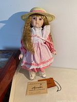 Full view of porcelain collector doll 'Sarah' in pink dress and bonnet, standing with certificate of authenticity visible.