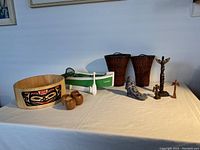 Full view of the lot items arranged on a flat surface showing the wooden serving bowl with indigenous design, napkin holders, wall pockets, wolf sculpture, cast totem poles, and replica boat with paddle and net.