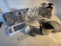 Overview of all kitchenware items on white cloth including kettle, strainers, graters, timer.