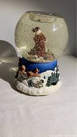 Front and side views of musical holiday snow globe depicting Santa Claus inside globe and winter scene with reindeer and sleigh on base.