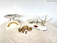 Pair of vintage and antique kitchen scales with weights on cloth surface, bright lighting, white background