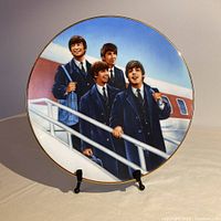 Front view of the round porcelain plate featuring a detailed colored image of The Beatles walking up airplane stairs, rimmed with gold.