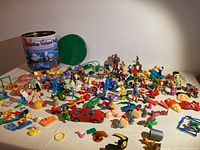 Photo showing a variety of small toys spread out including characters from animated series and small plastic figures along with the metal tin container.