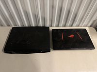 Two closed gaming laptops side by side showing Alienware logo on left unit and ROG logo on right unit