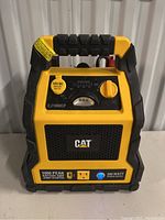 Front view of the yellow and black CAT CJ1000CP jump starter showing 12V DC outlet, control dial, and branding.
