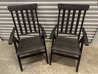 Two dark brown wooden IKEA patio chairs side by side with slatted back and seat, armrests, foldable design.