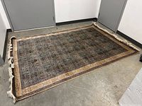 Full view of large rectangular rug on concrete floor showing complete item and fringed edges