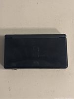 Closed view of black Nintendo DS Lite handheld console showing top shell with embossed logo.