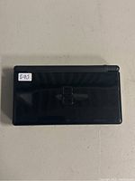 Closed top view of the black Nintendo DS Lite showing the exterior surface and hinge, with a small price sticker of $90.