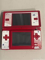 Front open view of red and white Nintendo DS Lite with Mario themed star design on faceplates and control keys.