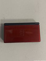 Closed red Nintendo DS Lite handheld gaming console showing slightly worn red metallic outer shell with Nintendo DS logo on top.