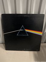 Front view of Pink Floyd 'Dark Side of the Moon' record sleeve showing iconic prism with white light beam and rainbow spectrum on black background. Minor scratches and wear visible.