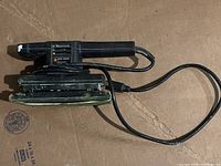 Full view of Black & Decker finishing sander with attached power cord, placed on cardboard surface.