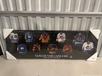 Rectangular black display case featuring nine miniature Vancouver Canucks hockey jerseys representing different eras inside with protective corner guards on the frame.