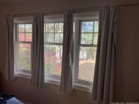 Four light beige curtain panels hanging on three window frames, showing full length and width coverage.
