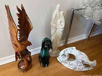 Photo showing all four figurines together, including wooden eagle, mother and child ceramic figurine, black and green ceramic dog, and abstract white ceramic sculpture