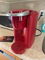 Front view of red Keurig K-Compact coffee maker with manual on countertop.