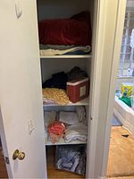 View of linen closet showing shelves filled with folded blankets, towels, and a boxed item