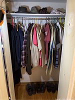 Closet rod with hanging men's clothing including jackets, shirts, hoodies, and pants in various colors and sizes L to 2XL, also hats and gloves on the shelf above.