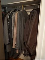 Closet view of men's suits, jackets, and coats on hangers showing variety of colors and fabrics.
