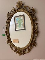 Full view of the oval hall mirror with ornate gold plastic frame hanging on a wall, showing its size and shape.
