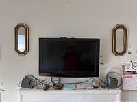 Two octagonal framed mirrors mounted on the wall on either side of a TV. The mirrors have a gold and brown multi-layered frame and measure 18x8 inches.