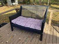 Outdoor black woven loveseat with cushion taken on wooden deck showing front angle.