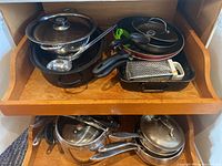 Photo showing assorted pots, pans, grater, and ladle organized on a wooden shelf.