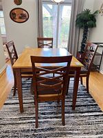 Full view of rectangular wood and laminate dining table with four matching wooden chairs with criss-cross backrest design around it on area rug.