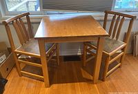 Photo showing the wooden square breakfast nook table with two matching chairs under windows, detail on wear and surface condition.