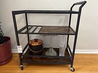 Full front view of metal and wood tea and serving cart with glass top and caster wheels, with some items on the lower shelf not included in sale.