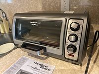 Front and side view of Hamilton Beach Easy Reach Toaster Oven on countertop with manual in front.