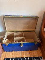 Photo of open blue metal storage trunk showing interior compartments and wear on metal fittings.