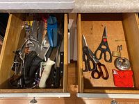 View of two open drawers showing various kitchen knives, scissors, padlocks, and a metal paper towel stand.