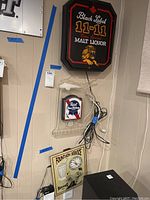 Photo showing the three advertising lights mounted on a wall: Black Label 11-11 Malt Liquor, Pabst Blue Ribbon light in clear plastic housing, and Fountain Service light with integrated clock.