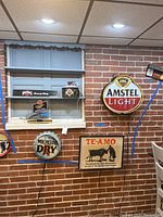 Full view of seven advertising items displayed on brick wall, including round lighted signs for Amstel Light, Michelob Dry, a Te-Amo plaque, and other illuminated signs.
