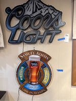 Front view of Coors Light illuminated sign and Samuel Adams seasonal beer sign mounted on wall.