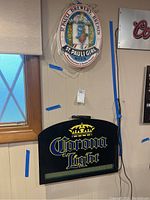 St Pauli Girl and Corona Light advertising light signs installed on wall with visible cords.