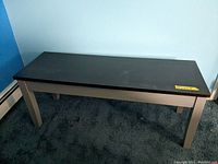 Front view of laminated wood look storage bench showing dark tabletop and light legs on carpeted floor.