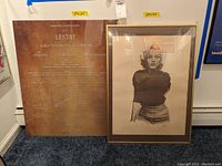 Two framed prints and movie poster leaning against the wall on blue carpet. The movie poster is the largest item showing the film Lestat credits.
