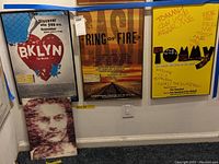 Three framed posters displayed on a wall with a framed book/artwork resting against the wall, showing lot contents