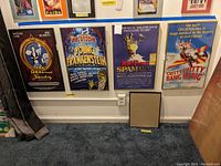 Photo showing four framed posters from musicals The Addams Family, Young Frankenstein, Spamalot, and Chitty Chitty Bang Bang, plus one empty frame leaning against the wall.