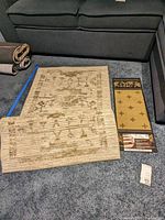 Threshold rubber backed runner laid flat with visible floral and geometric beige/light brown design, accompanied by rubber backed stair tread with fleur-de-lis pattern