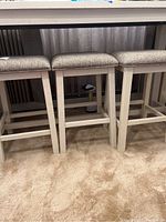 Group of three stools with white painted legs and light upholstered seats underneath a counter