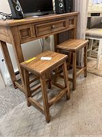 Front view of wood-like table and two stools, showing the drawer and stool seat tops.